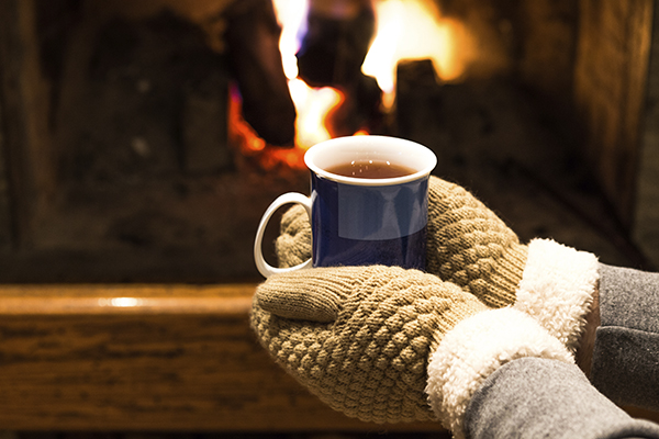 Hot tea in hands and fireplace background